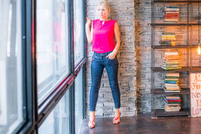 Woman looking through widow while standing against wall