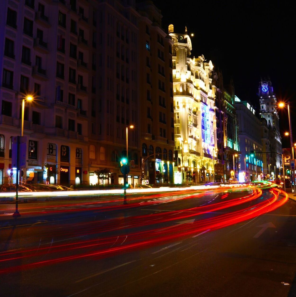 LIGHT TRAILS ON ROAD AGAINST BUILDINGS AT NIGHT