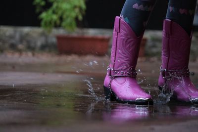 Low section of woman girl pink cowboy boot on wet street