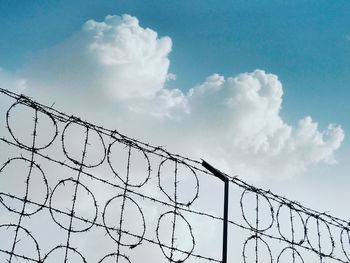 Low angle view of barbed wire fence against cloudy sky