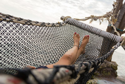 Low section of woman relaxing on rope against sea