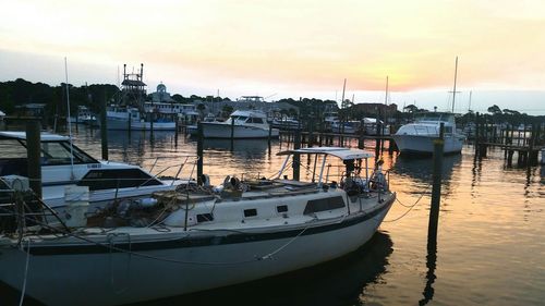 Sailboats moored on harbor against sky at sunset