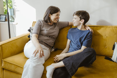 Smiling woman talking with son while sitting on sofa at home