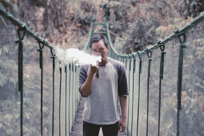 Portrait of young man standing on fence against trees