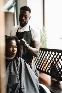 Male hairdresser cutting hair of female customer in barber shop