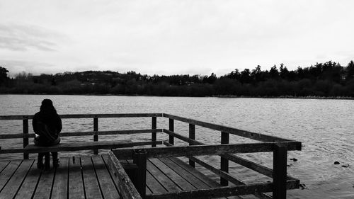 Rear view of man sitting on bench at lakeside