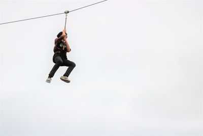 Low angle view of teenage boy zip lining against sky