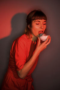 Young woman holding red drink against gray background