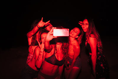 Cheerful women doing selfie while standing in dark