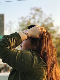 Side view of woman with hand in hair standing outdoors