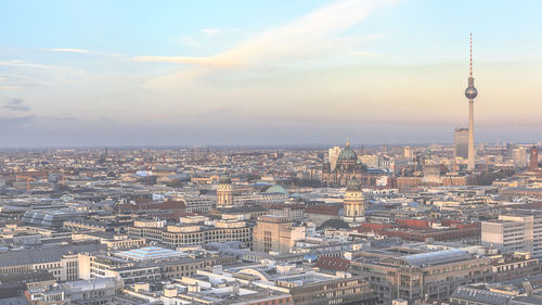 Fernsehturm amidst cityscape against sky during sunset