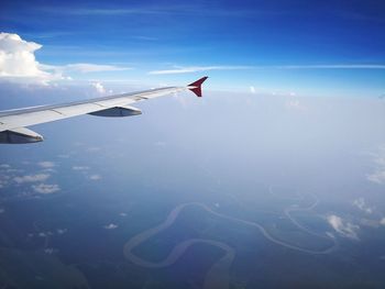 Cropped image of airplane wing flying over landscape against blue sky