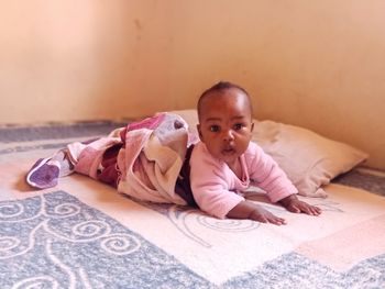 A baby. lying on stomach. peach wall. looking at camera. pink. white. blue. 