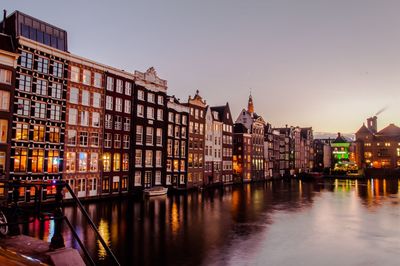 River by illuminated buildings against clear sky at dusk