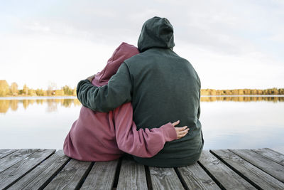 Senior man embracing granddaughter on jetty in front of lake