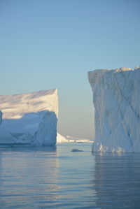 Scenic view of frozen sea with icebergs against clear sky in midnight sun