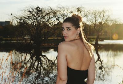 Portrait of beautiful woman standing by lake against trees