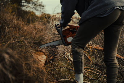Teenage boy cutting wood with chainsaw in forest