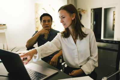 Businesswoman discussing with male colleague over laptop while sitting at office