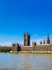 Buildings by river against blue sky in city