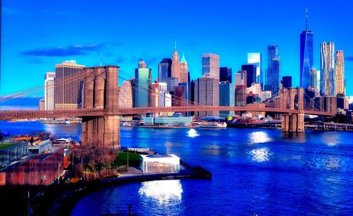 Bridge over river by buildings in city against blue sky