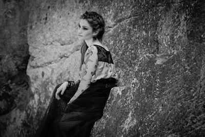 Woman looking away while sitting against rocks