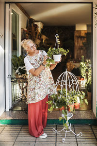 Blond female florist checking potted plant at flower shop entrance