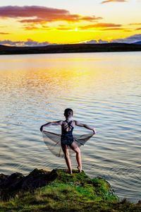 Rear view of girl posing at lakeshore during sunset