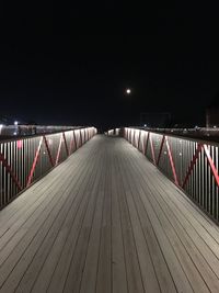 Empty footbridge leading to pier at night