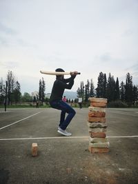 Full length of man playing cricket on road against sky