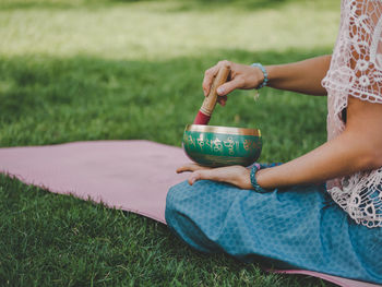 Midsection of young woman holding bowl while sitting on grassy field