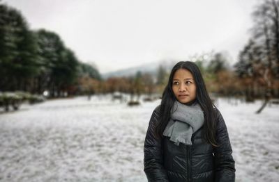 Woman looking away while standing outdoors in winter