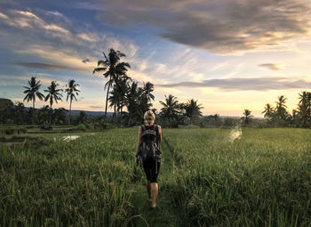 Rear view of woman standing on field against sky during sunset