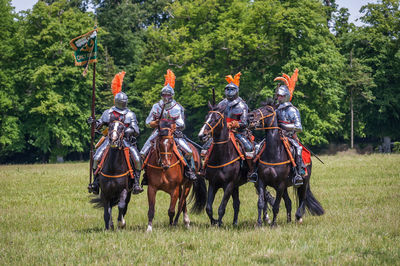 Men riding horses on field against trees