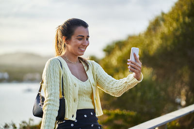 Smiling young woman using phone while standing outdoors
