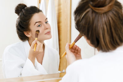 Woman applying make-up in bathroom