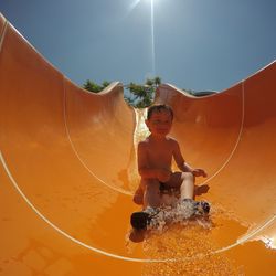 Low angle view of shirtless boy on water slide against clear sky