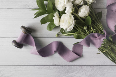 White flowers tied with mauve linen ribbon laying on white boards
