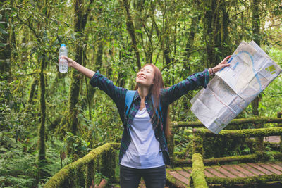 Full length of woman with arms raised standing in forest