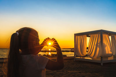 Rear view of woman on beach against sky during sunset