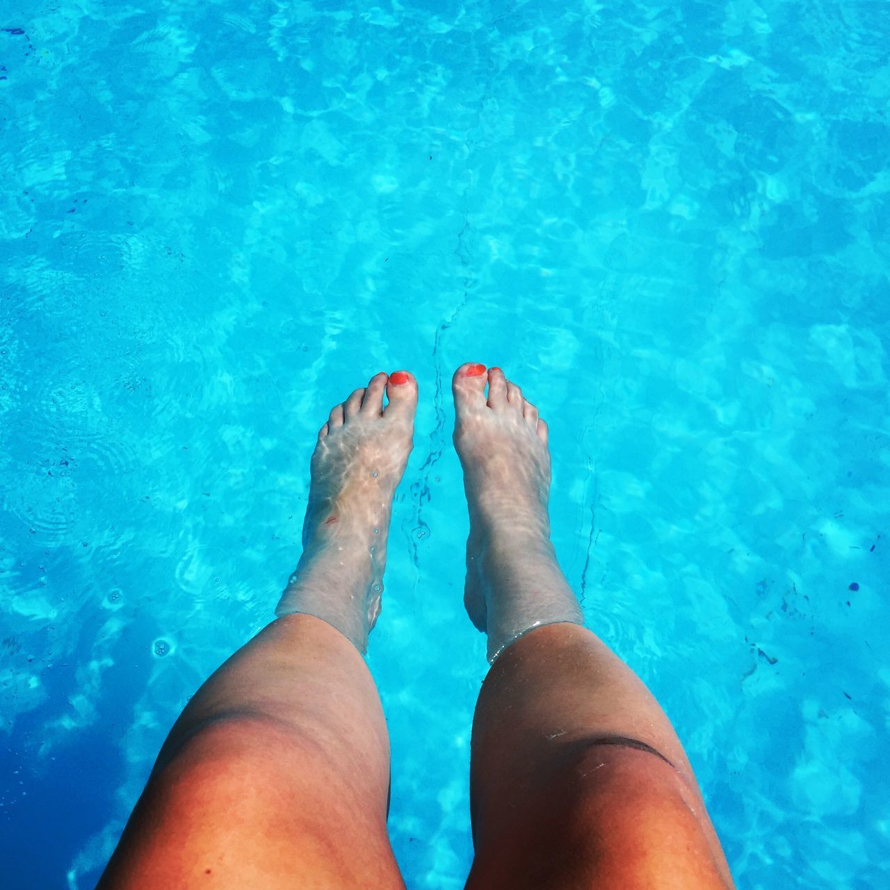 low section, person, personal perspective, water, human foot, barefoot, swimming pool, blue, lifestyles, leisure activity, high angle view, turquoise colored, relaxation, wet, part of, nail polish