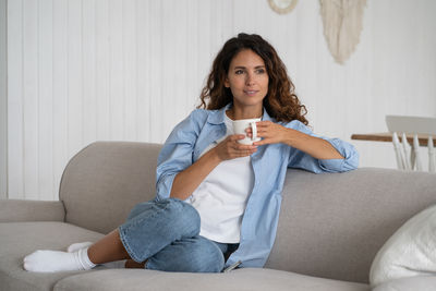 Young woman using mobile phone while sitting on sofa at home