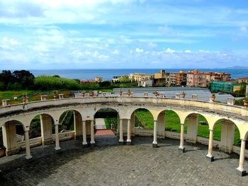 Bridge over river by buildings against sky