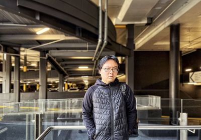 Portrait of young asian man standing at railings against building features.