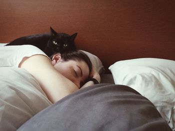 Portrait of cat lying by woman sleeping on bed at home