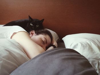 Portrait of cat lying by woman sleeping on bed at home