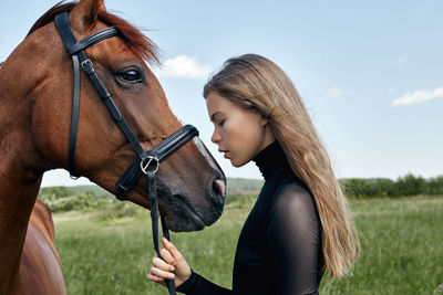 Side view of young woman with horse standing on field