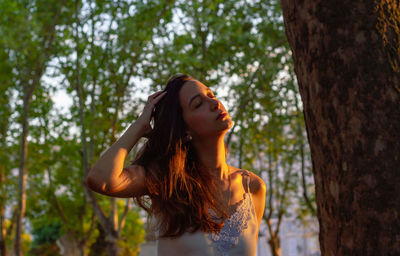 Young woman looking away while standing against tree