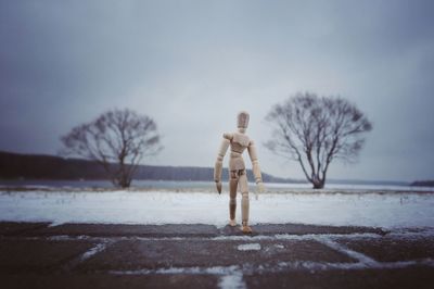 Wooden figurine on footpath against sky during winter