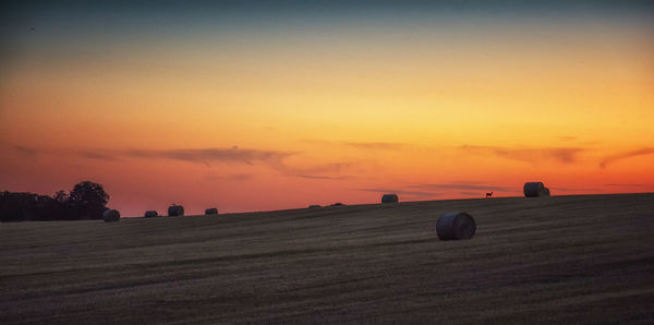 Hay bales on field against sky during sunset